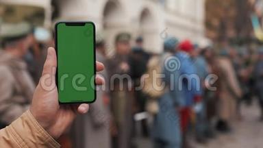 一名男子手持一部移动电话的特写镜头，街道上有一个垂直的绿色屏幕。大屏幕。军事