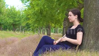 一个年轻漂亮怀孕的女孩穿着一件黑色T恤坐在树下