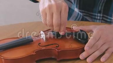 穿格子衬衫的年轻人的特写双手正在修理坐在桌子旁的小提琴。 拧开螺栓