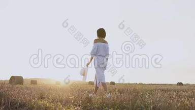 穿着帽子的女孩沿着草田散步。 一个穿着蓝色连衣裙的女人带着草捆在田野上。 一个女孩