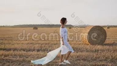 侧视。 美丽迷人的女人在田野上奔跑，围巾在风中飘扬。 自由概念