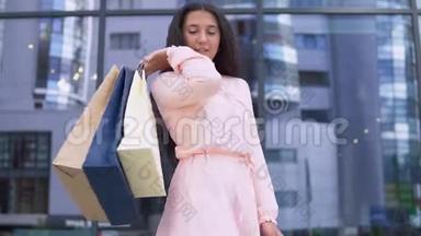 年轻的女孩在买完衣服后，手里拿着包裹，对购买很满意。 慢动作。 高清高清
