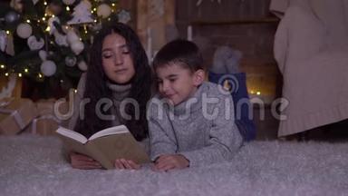 留着长发的妈妈给儿子读一本书，并在圣诞节的时候亲吻他躺在圣诞树附近的地板上。 <strong>高清高清</strong>