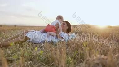 年轻的女人和小男孩在大自然上快乐地玩耍。 躺在地里的母亲把婴儿抱在<strong>怀里</strong>，