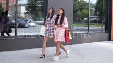 两个年轻的快乐女孩在购物中心附近购物后拿着购物袋。 慢动作。 高清高清