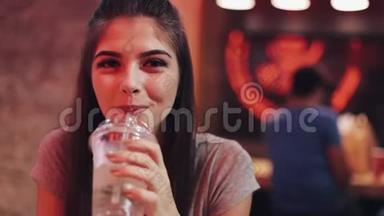 年轻女子坐在酒吧里，喝着莱曼纳德，看着镜头。 在交流中享受夜生活的女人