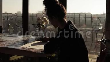女艺术家坐在桌子旁，桌上放着鲜花，用笔在纸上画，在一个极简约的艺术工作室里