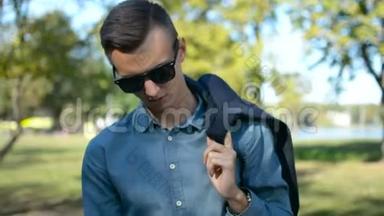 一位年轻的商人在阳光明媚的日子里用他的手机智能手机在外面等着的画像