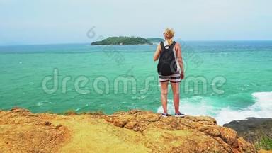 旅游女孩站在悬崖边，看着海浪与热带海滩。 美丽的海景。 夏季