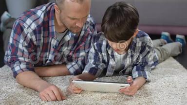 男孩在平板电脑上使用交互式应用程序，在父亲的帮助下，家庭时间