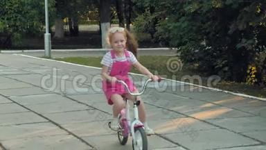 一个快乐、美丽、金发碧眼的小女孩穿着粉红色的裙子，跳投骑着一辆儿童`自行车上路