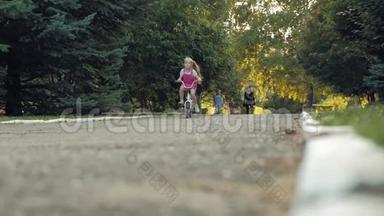 一个快乐、美丽、金发碧眼的小女孩穿着粉<strong>红色</strong>的裙子，跳投骑着一辆<strong>儿童</strong>`自行车上路