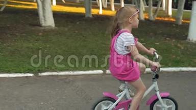 一个快乐、美丽、金发碧眼的小女孩穿着粉红色的<strong>裙子</strong>，跳投骑着一辆<strong>儿童</strong>`自行车上路