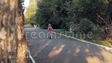 一个快乐、美丽、金发碧眼的小女孩穿着粉红色的裙子，跳投骑着一辆儿童`自行车上路
