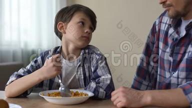 可怜的小男孩用勺子搅拌玉米片，看着父亲，<strong>胃口</strong>很差