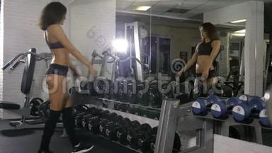 一个穿着<strong>运动服</strong>、穿着<strong>运动服</strong>的女孩在一面镜子旁边转过身，看着她的运动健