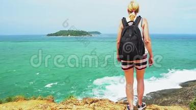 一个背着背包的旅行者女孩站在沙滩上，望着远方。有岩石和大海的美丽海景