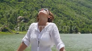 幸福的女人享受河山覆盖的绿色森林。 美丽的女孩在湖岸放松，仰望天空