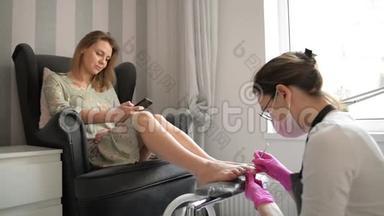 美丽的女人在水疗美容沙龙获得专业教育。 师父正在清洗她的指甲。 客户正在聊天