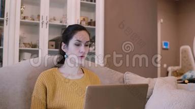 年轻<strong>女子坐在沙发上</strong>拿着笔记本电脑。 女有视频电话会议，在网上聊天..