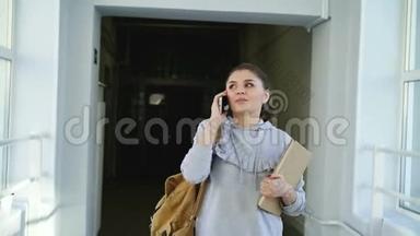 多莉拍摄的美丽美丽的女学生走在大学走廊上，拿着<strong>课本</strong>在电话交谈