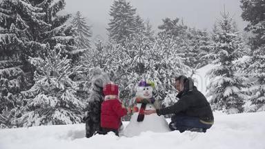 一家人在公园里堆雪人，可爱的孩子固定纽扣，下雪的树，美丽的冬天的家庭肖像，真正的团队合作