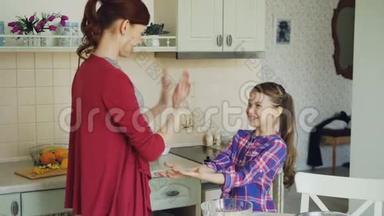 快乐的妈妈和可爱的有趣的女儿玩拍手游戏，在家厨房做饭时玩得很开心。 家庭
