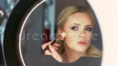 一个美丽优雅的金发女人在镜子前给<strong>自己做</strong>了一个迷人的晚妆。