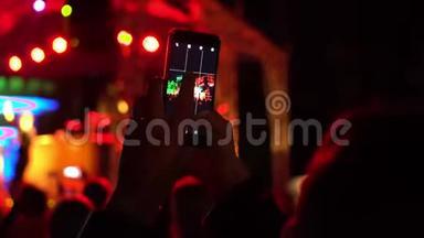女孩在智能手机上录制音乐会，一大群快乐的人欣赏摇滚音乐会，举起双手鼓掌