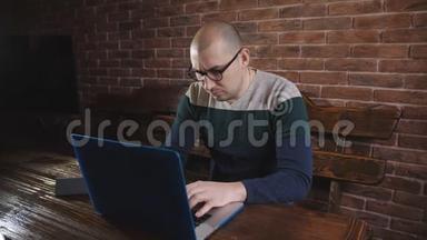 戴眼镜的人热衷于在笔记本电脑上工作。 一位男作家正在笔记本电脑键盘上打字。