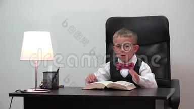 疲惫的孩子坐在办公桌前，头靠在书上<strong>睡</strong>觉，滑稽的肖像，小瞳孔和大眼镜，失去了童年