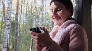 秋天森林里的快乐女人在电话上交谈，在智能手机上发送信息，在手机上读一些东西