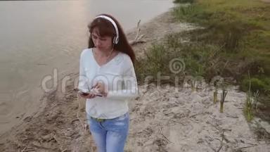 带着耳机的<strong>女孩</strong>走在水旁边的沙子上，在平板电脑上<strong>听音乐</strong>。 <strong>女孩</strong>在海滩上散步和支票