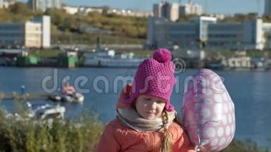 小女孩戴着粉红色的帽子，带着气球坐在河港上，一边旅行，一边微笑