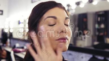 化妆师`在一个漂亮的深褐色头发的女孩的脸上涂上粉底的过程