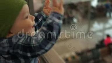 一岁的孩子用钢笔敲玻璃，看着机场候车室。 父亲抚养孩子