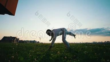 强壮的人在草地上训练，在夏天的晚上表演卡波伊拉舞