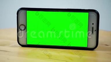 智能手机用铬键旋转，绿色屏幕。 阿尔法视频，木制背景上的手机。 模拟视频