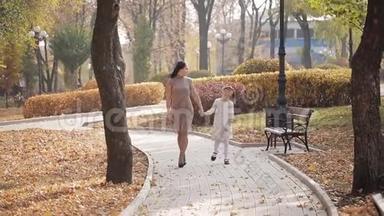 妈妈和女儿正沿着一条布满秋黄树叶的大道走着。 一家人在城市<strong>公园散步</strong>