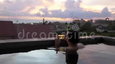 年轻人用智能手机在游泳池休息和喝啤酒时拍摄美丽的日落。 慢动作