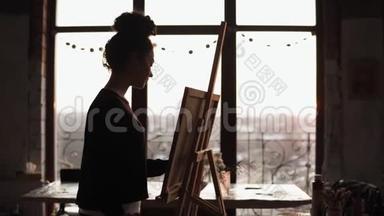 年轻受启发的专业女艺术家把CanCas放在画架上，在画架上涂上油漆，然后开始画画。