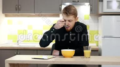 带着平板电脑的年轻人坐在厨房的<strong>桌子</strong>旁吃<strong>早餐</strong>。