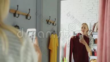 女客户正在用智能<strong>手机制作</strong>新针织跳线的镜面自拍。 她站在房间里