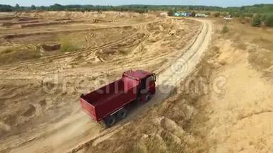 夏季，红色自卸卡车在靠近森林的采石场的沙路上行驶的鸟瞰图。 场景。 工业