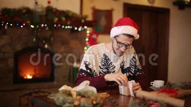 戴着圣诞帽的快乐男人在壁炉旁<strong>打开</strong>圣诞<strong>礼物盒</strong>，里面有闪烁的花环。 微笑的家伙收到了