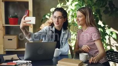 年轻的企业家在现代办公室里坐在办公桌前用智能手机聊天和自拍。 他们是