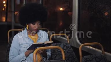 年轻的非裔美国妇女或坐在公共交通工具上的乘客读物，ste dicam拍摄。 慢动作。 城市