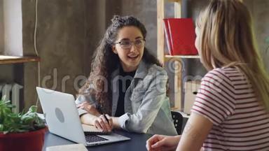 小企业的年轻老板正在现代办公室和她的客户交谈。 女人们坐在办公桌前聊天