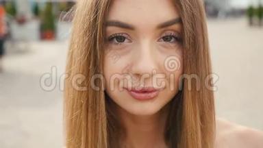 脸浅棕色头发的年轻女人看着镜头近距离。 城市街头背景的肖像美女