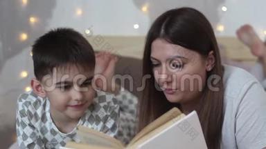 一位留着长发的美丽母亲给躺在床上的小男孩读了一本书，吻了他一个好心情。 高清高清